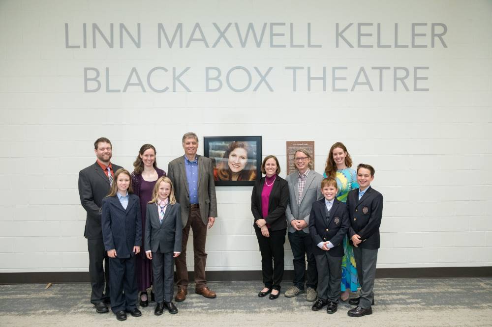 The family is posing in front of the photo of Linn Maxwell Keller.